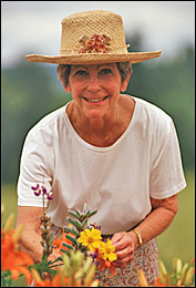 Picture of a 72 year old woman in a straw hat, tending flowers in her garden.